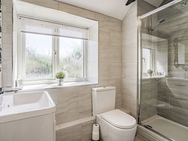 A bathroom with a toilet sink window and a glass shower enclosure at Granary Cottage in Pembroke