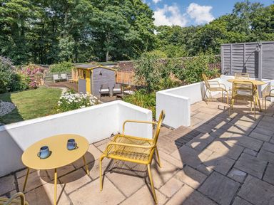 An outdoor patio with yellow chairs and tables overlooking a garden with a shed at Granary Cottage in Pembroke