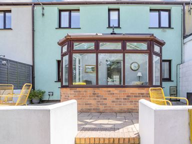 A backyard patio with yellow chairs and a conservatory attached to a light green house at Granary Cottage in Pembroke