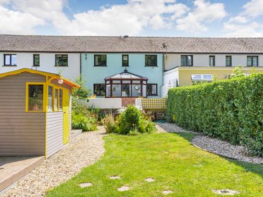 A backyard garden with a pathway gravel and a wooden shed next to a row of terraced houses at Granary Cottage in Pembroke