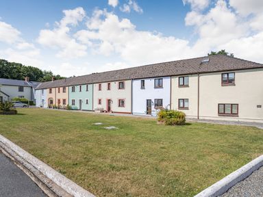 A row of pastel colored terrace houses with small front gardens and benches on a lawn at Granary Cottage in Pembroke