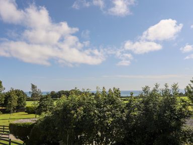 A landscape with trees and grass fields under a partly cloudy sky at Gorwel in Moelfre