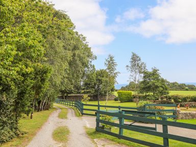 A gravel driveway with green wooden fences and trees on the left side at Gorwel in Moelfre
