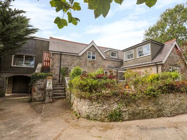 An exterior view of a stone house with greenery and plants around it at Gorwel in Moelfre
