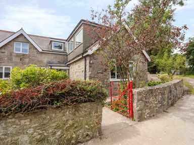 Stone house with multiple windows and a red gate with bushes and trees around at Gorwel in Moelfre