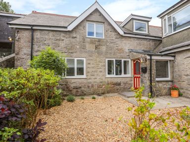 A stone exterior house with a red door gravel front yard and green bushes at Gorwel in Moelfre