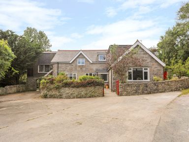 Stone house with multiple windows a concrete driveway and trees at Gorwel in Moelfre