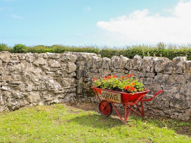A red wheelbarrow with flowers next to a stone wall at Gorwel in Moelfre