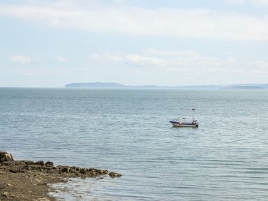 A small boat moored on calm water near a rocky shore with distant land visible at Gorwel in Moelfre