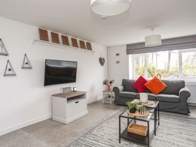 A living room with a grey sofa with red and orange cushions and a TV on the wall at Gorwel in Moelfre