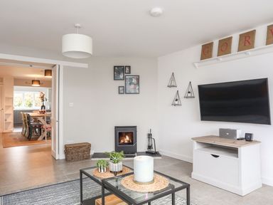 A living room with a fireplace a glass coffee table a wall mounted television and a wicker basket at Gorwel in Moelfre
