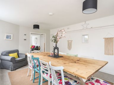 A dining room with a wooden table surrounded by chairs with floral cushions and a grey armchair with a yellow cushion at Gorwel in Moelfre