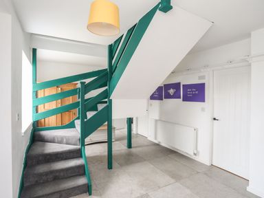 A staircase with green railings and grey carpet in a hallway with white walls and a closed white door at Gorwel in Moelfre