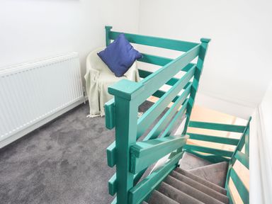 A stairway with green railings and a corner with a chair covered with a blanket and a blue pillow at Gorwel in Moelfre