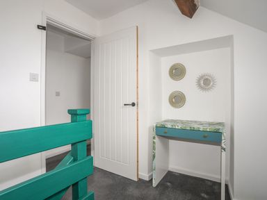 A hallway with a teal wooden railing a floral patterned desk and three round wall mirrors at Gorwel in Moelfre