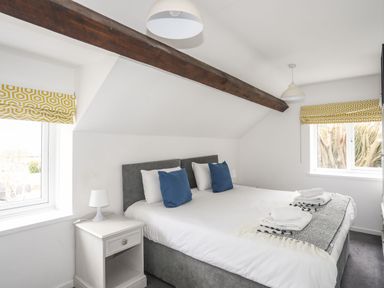 A bedroom with a double bed blue pillows and white bedside tables at Gorwel in Moelfre