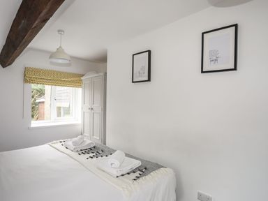 A bedroom with a bed, folded towels on a blanket, a window with patterned blinds, a wardrobe, and framed pictures on the wall at Gorwel in Moelfre