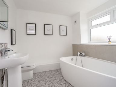 A bathroom with a bathtub sink toilet framed pictures and a window at Gorwel in Moelfre