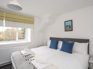 A bedroom with a large bed blue pillows folded towels bedside lamp and a window with patterned blinds at Gorwel in Moelfre