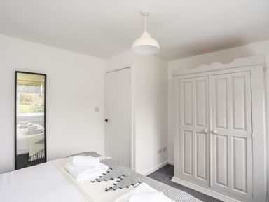 A bedroom with a bed folded towels a wardrobe a wall mirror and a door at Gorwel Moelfre