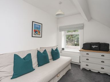 A small living room with a beige sofa with teal cushions a dresser a window and a framed picture on the wall at Gorwel in Moelfre