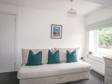 A room with a beige sofa with teal pillows a framed picture on the wall a window and a white door at Gorwel in Moelfre
