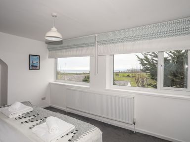 A bedroom with a bed and towels near windows with a view of fields at Gorwel in Moelfre