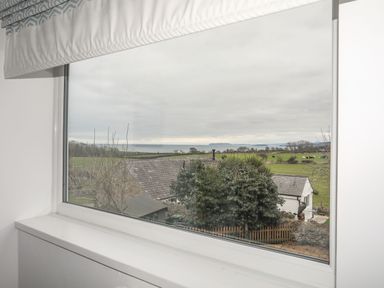 A window with a view of houses trees fields and the sea at Gorwel in Moelfre
