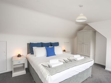 A bedroom with a double bed blue and white pillows bedside tables with lamps and a wardrobe at Gorwel in Moelfre
