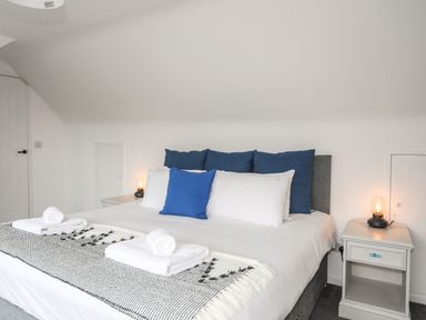 A bedroom with a bed featuring blue and white pillows and two bedside tables with lamps at Gorwel in Moelfre