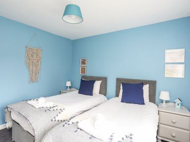 A bedroom with two single beds with blue pillows and white bedding at Gorwel in Moelfre