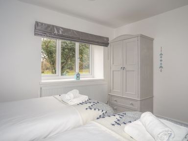 A bedroom with two single beds with towels near a window and a wardrobe at Gorwel in Moelfre
