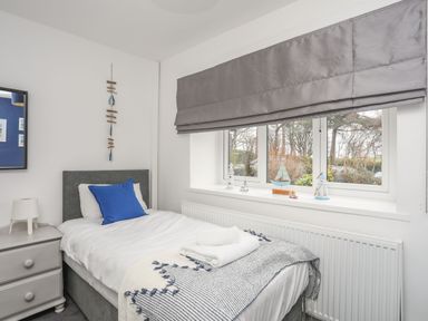 A bedroom with a single bed next to a window with small boat decorations at Gorwel in Moelfre