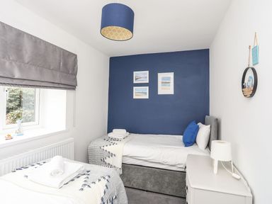 A bedroom with two single beds a blue accent wall with framed pictures and a white bedside table with a lamp at Gorwel in Moelfre