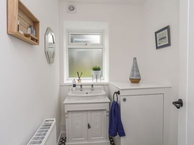 A small bathroom with a sink under a frosted window a cabinet a blue towel and a wall mirror at Gorwel in Moelfre