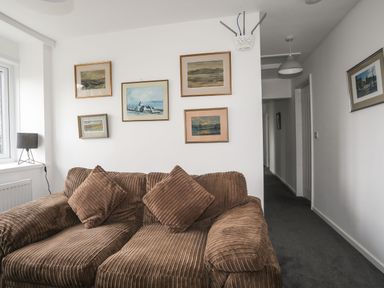 A brown corduroy sofa with cushions under framed pictures on a white wall at Gorwel in Moelfre