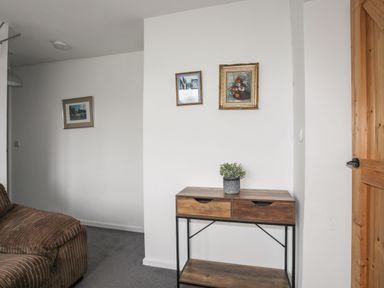 A corner of a room with a wooden and metal console table with a plant on it and two pictures on the wall at Gorwel in Moelfre