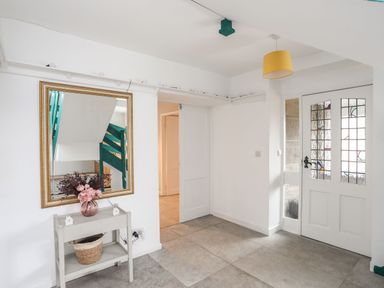 An entryway with a white door with glass panels a small table with a basket and flowers and a large mirror reflecting a green staircase at Gorwel in Moelfre