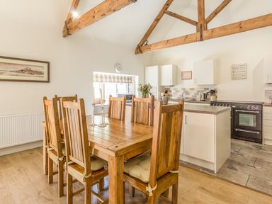 A kitchen with wooden dining table and chairs and exposed wooden ceiling beams at Sawmill Cottage in Belford near Bamburgh