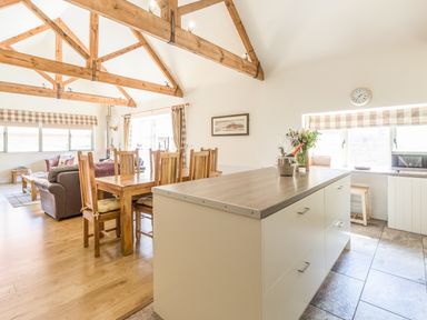 An open living and dining area with wooden beams on the ceiling and a kitchen island with flowers and a bottle on it at Sawmill Cottage Belford near Bamburgh