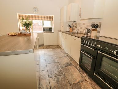 A kitchen with black oven and stove white cabinets microwave and window with checked blind at Sawmill Cottage in Belford near Bamburgh