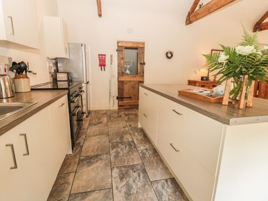 A kitchen with a stove refrigerator island countertop wooden door and flowers at Sawmill Cottage in Belford near Bamburgh