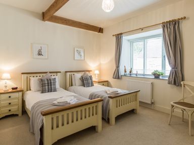 A bedroom with two single beds bedside tables and a window with curtains at Sawmill Cottage in Belford near Bamburgh