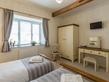 A bedroom with two single beds a wardrobe a dressing table a chair and a window at Sawmill Cottage in Belford near Bamburgh