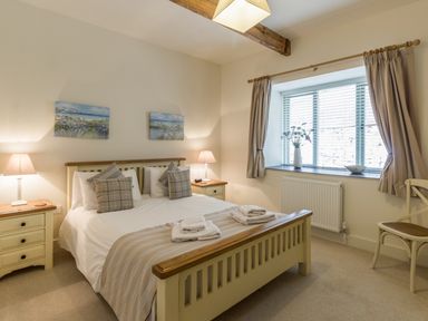 A bedroom with a double bed bedside tables lamps and a window with curtains at Sawmill Cottage in Belford near Bamburgh