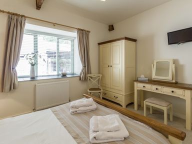 A bedroom with a bed with folded towels a wardrobe a dressing table with a stool a chair and a window with curtains at Sawmill Cottage in Belford near Bamburgh