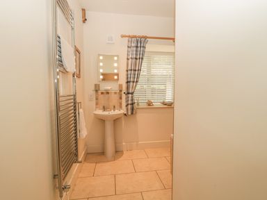 A bathroom with a pedestal sink a wall-mounted mirror a window with blinds and a curtain and a towel radiator at Sawmill Cottage Belford near Bamburgh