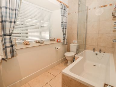 A bathroom with a bathtub shower toilet window with blinds and blue check curtains at Sawmill Cottage Belford near Bamburgh