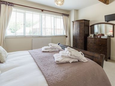 A bedroom with a bed covered with a knitted blanket and bathrobes on it next to a wardrobe and a dresser with a mirror at Sawmill Cottage in Belford near Bamburgh