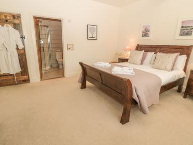 A bedroom with a wooden bed and beige carpet and an en suite bathroom at Sawmill Cottage in Belford near Bamburgh